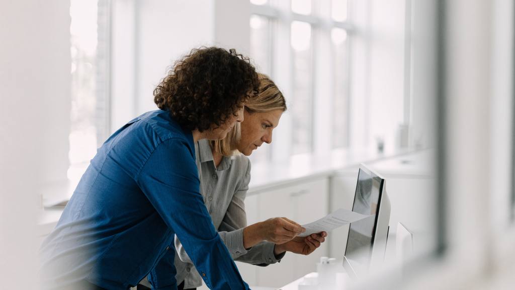 Due colleghe verificano insieme un documento davanti a un monitor